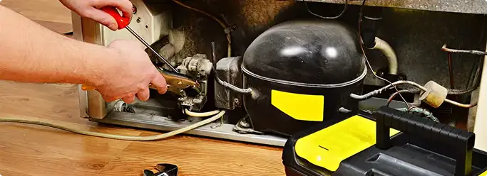 Refrigerator repair technician fixing the compressor and wiring in East Providence, RI