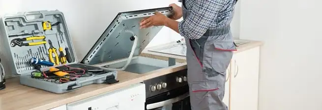 Cooktop repair technician lifting a built-in stovetop for service in Providence, RI