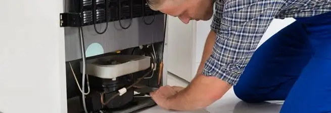 Refrigerator repair technician servicing the compressor and condenser area in Providence, RI