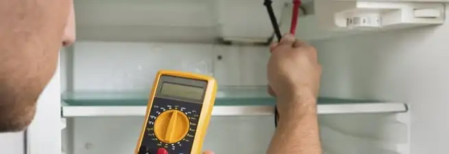 Refrigerator repair technician testing electrical components with a multimeter in Providence, RI